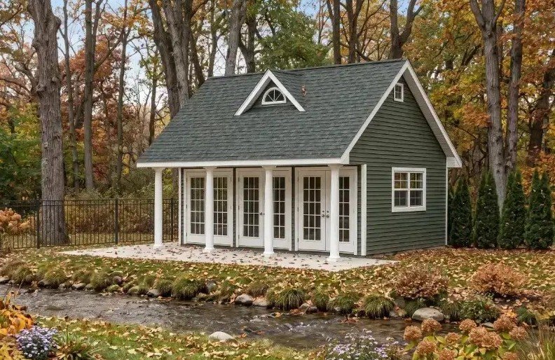 Premium Appalachian pool house with deep green lap siding, white trim, covered porch, multiple French doors, and a landscaped creekside setting